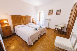Une chambre avec deux lits, une chaise, une table de chevet, une lampe et un radiateur.
