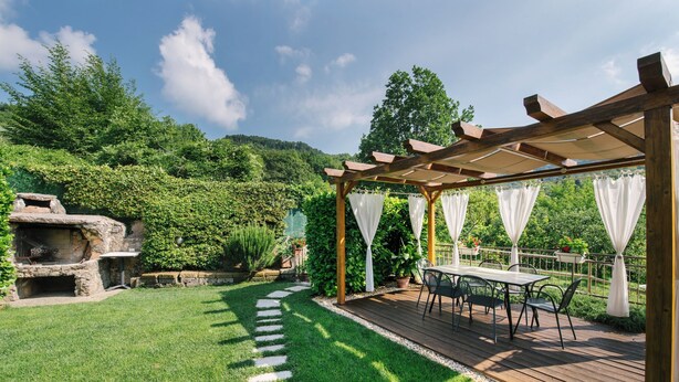 Une terrasse en bois agrémentée d’une pergola, d’un espace salon extérieur et d’une cheminée en pierre.