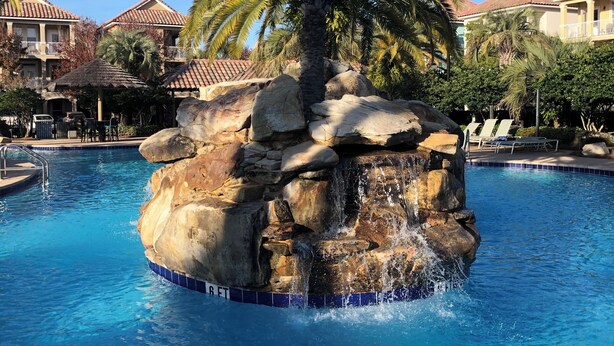 A pool with a rock feature and palm trees. - Spacious Destin home for families! Walk or free shuttle to beach, resort pool! (Destin)