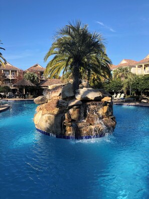 A pool with a rock feature and palm trees. - Spacious Destin home for families! Walk or free shuttle to beach, resort pool! (Destin)