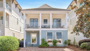 A two-story building with a covered patio, a brick pathway, and a small garden area. - Spacious Destin home for families! Walk or free shuttle to beach, resort pool! (Destin)