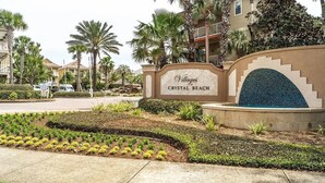 A sign for Villages Crystal Beach with a landscaped garden and palm trees. - Spacious Destin home for families! Walk or free shuttle to beach, resort pool! (Destin)