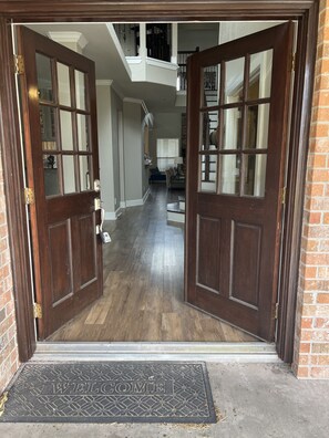 Entrada con puerta doble de madera, un felpudo de bienvenida y un vestíbulo con escalera y zona de estar.