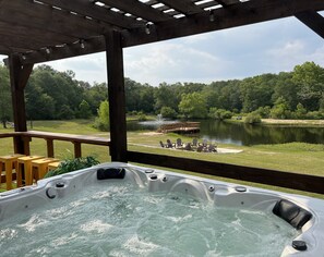 A hot tub with a view of a lake, deck chairs, and a wooden pergola.