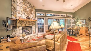 A cozy living room with a stone fireplace, leather sofas, a dining area with a table and chairs, and a ceiling fan.