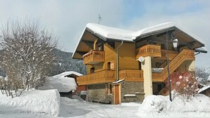 Un chalet en bois à deux étages, doté de balcons, entouré d’arbres couverts de neige et surplombant un ciel dégagé.