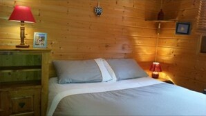 Une pièce aménagée comme un chalet en bois, avec un lit, une lampe rouge et une petite étagère sur laquelle est posé un cadre photo.