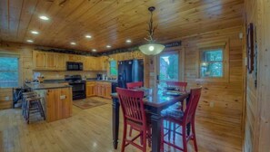 Une cabane en bois dotée d’une cuisine avec un îlot central, d’une table à manger avec des chaises et d’un plafond pourvu d’un éclairage encastré.