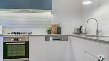 Una cocina moderna con armarios blancos, un lavavajillas Bosch, un horno Bosch, una estufa a gas y un tostador de acero inoxidable.