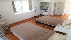A room with two beds, a small kitchenette, a window with curtains, and a door leading to another room. - Lagoon Palace (Kadena)
