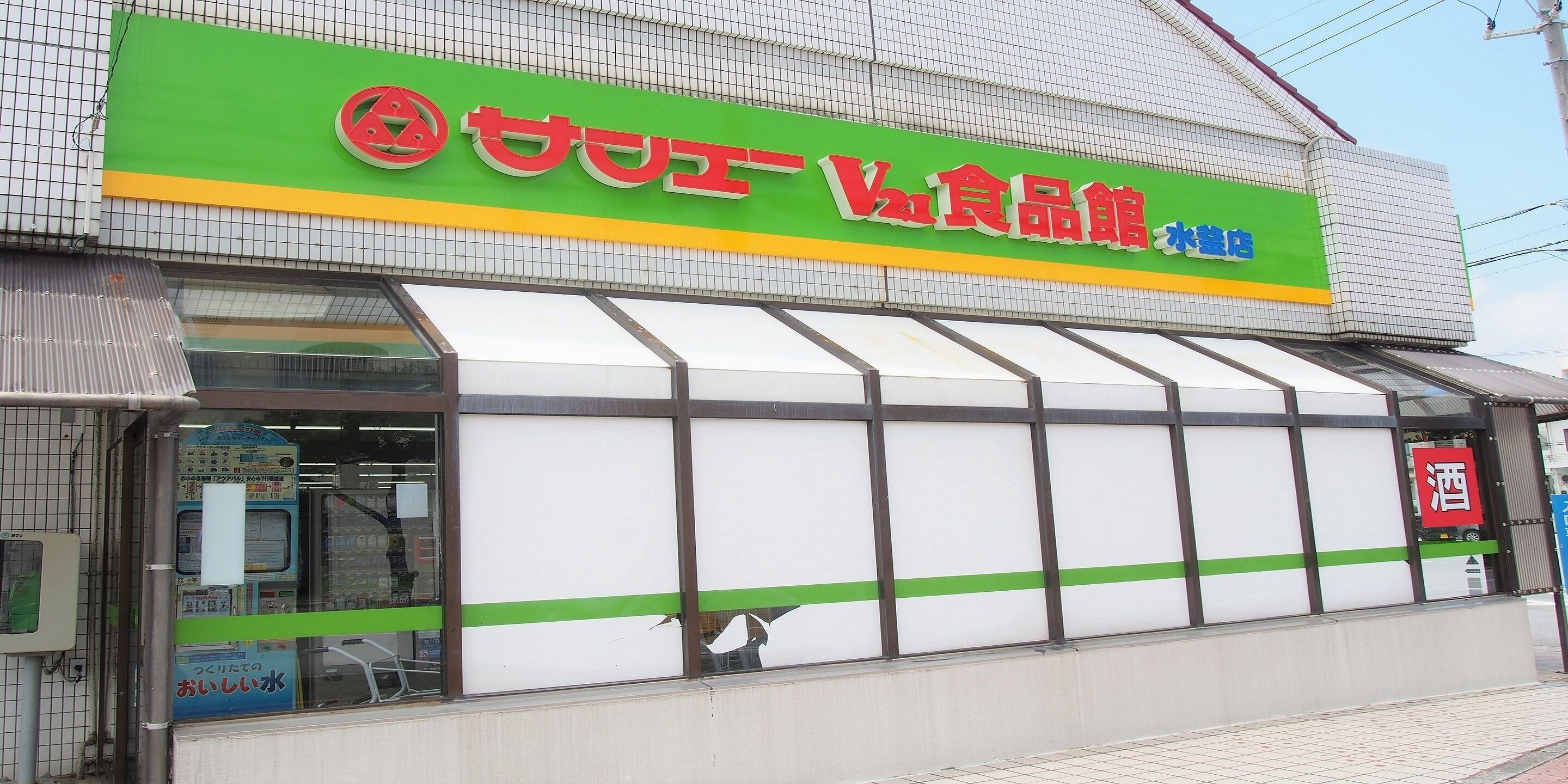 A storefront with a green and yellow sign, a large glass window, and a small awning.