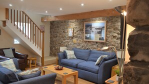 A living room with a stone wall, a blue sofa, a wooden coffee table, and a staircase. - The Hay Barn - Exclusive 2 bedroom stone cottage (Llyn Peninsula)