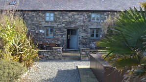 A stone house with a gravel driveway, a wooden bench, and a door. - The Hay Barn - Exclusive 2 bedroom stone cottage (Llyn Peninsula)