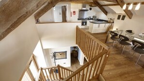 Un amplio apartamento tipo loft con techos altos, vigas de madera a la vista, una cocina con electrodomésticos modernos y una zona de comedor con sillas de diseño contemporáneo.