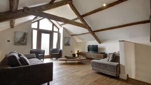 Un loft espacioso con vigas de madera a la vista, un ventanal grande y una zona de estar acogedora con un sofá y sillones.