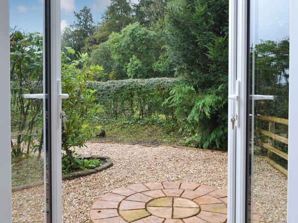 A view through glass doors of a garden area with gravel paths, a circular stone pattern, and lush greenery.