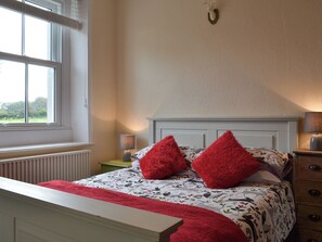 A bedroom with a bed, two red pillows, a white headboard, a window, and a lamp on a bedside table. - 2 bedroom accommodation in Waverton, near Wigton (Waverton, near Wigton)