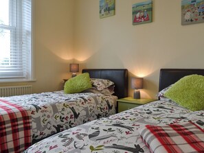 A bedroom with two beds, each with a green pillow and a patterned duvet. There are bedside tables with lamps and a window with blinds. - 2 bedroom accommodation in Waverton, near Wigton (Waverton, near Wigton)
