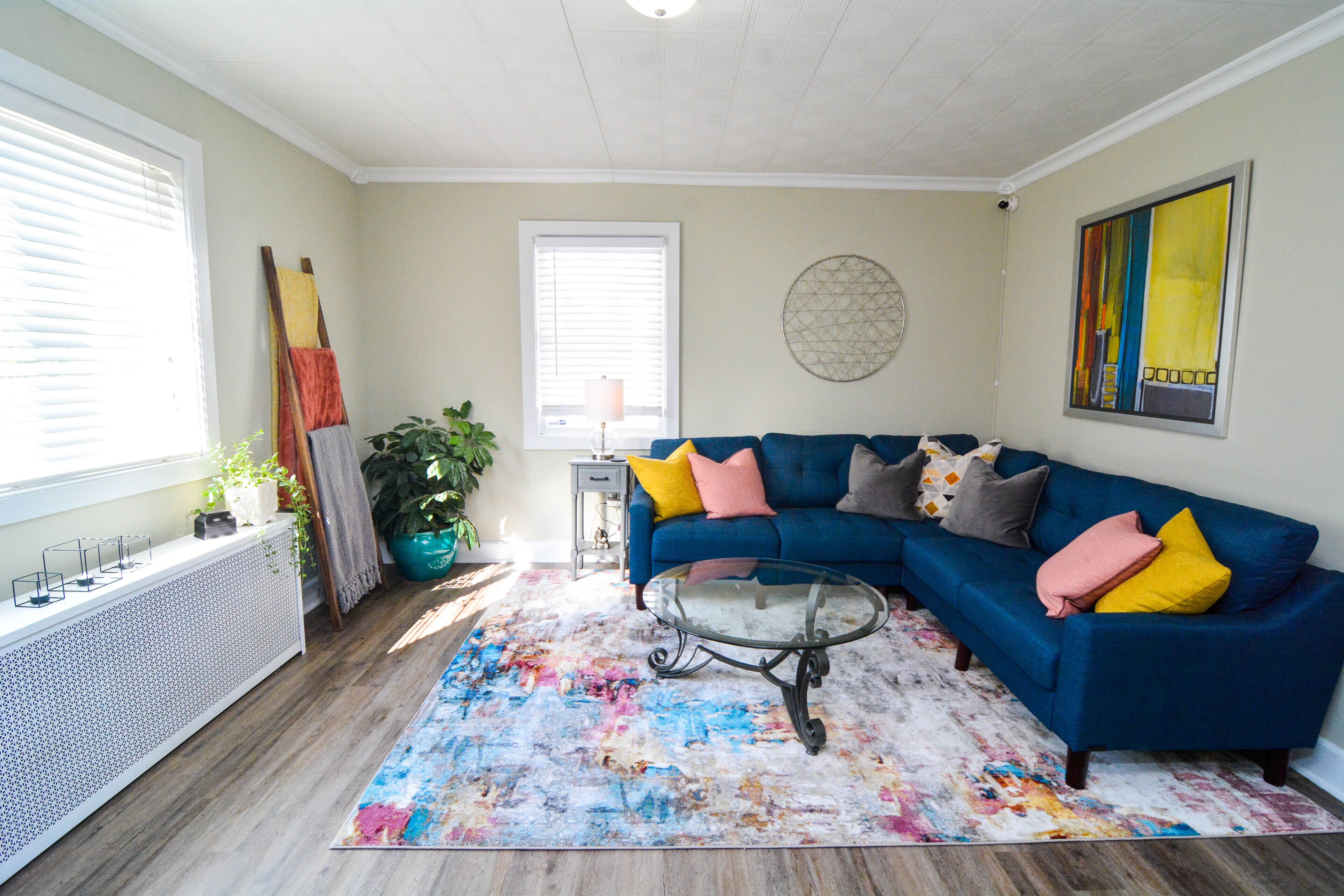 A living room with a blue sectional sofa, a glass coffee table, and a colorful rug.