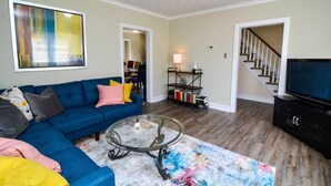 A living room with a blue sofa, a glass coffee table, a colorful rug, a TV, and a bookshelf. - Excellent Location, Family & Pet Friendly, Walk to Main St, Close to everything (Bethlehem)