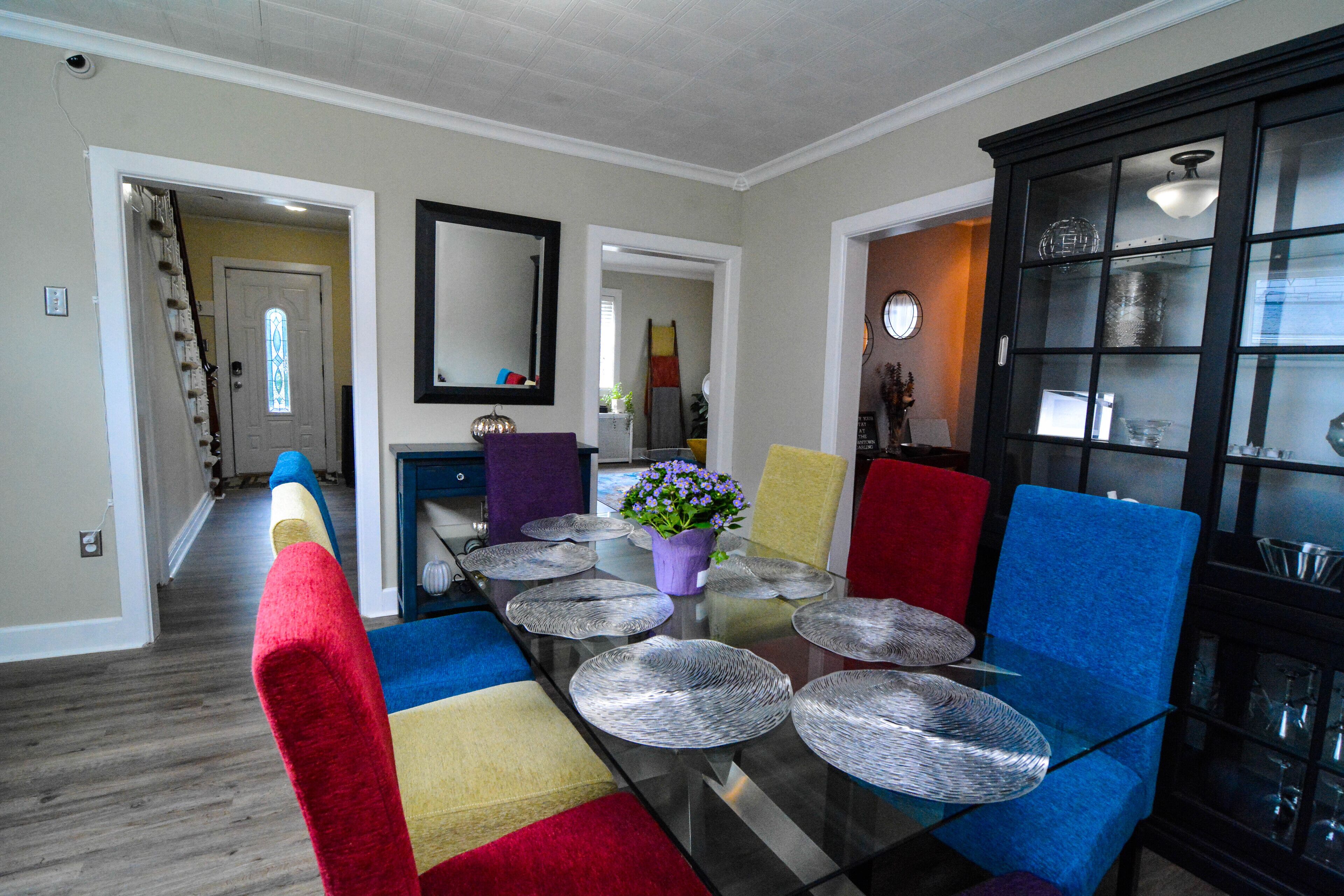 A dining area with a glass table, colorful chairs, and a black cabinet with glass doors.