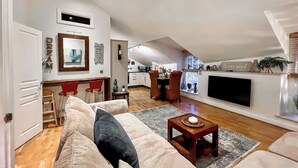 A cozy living room with a sofa, a coffee table, and a fireplace. There is a dining area with chairs and a kitchen in the background. - 2 bedroom accommodation in Fowey (Fowey)