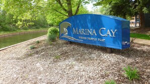 Un panneau bleu sur lequel on peut lire « MARINA CAY » et « WHERE PEOPLE PLAY », entouré d’arbres et bordé d’un chemin de gravier.