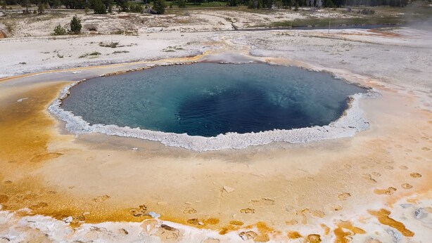 Une source thermale géothermique avec une piscine circulaire entourée de dépôts minéraux.