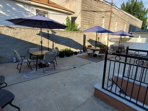 Eine Terrasse im Freien mit Tischen, Stühlen, Sonnenschirmen und Kübelpflanzen.