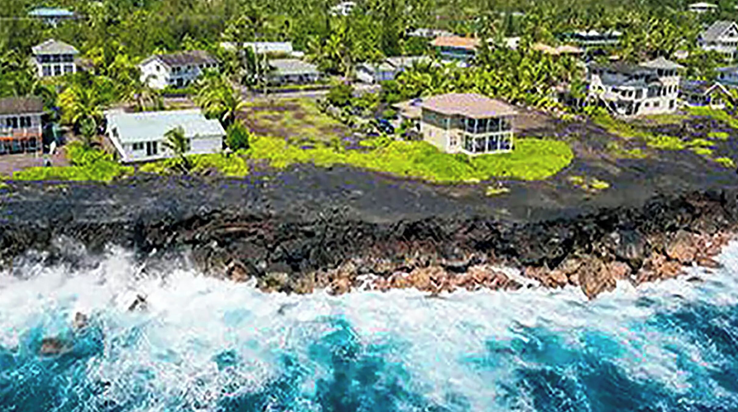A coastal property with houses on a lava field, surrounded by ocean waves.