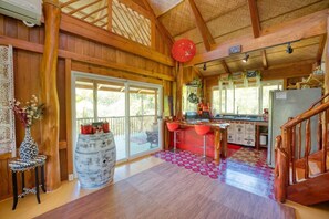 A rustic wooden interior with a kitchen area, a dining table with red chairs, and a large window providing natural light.