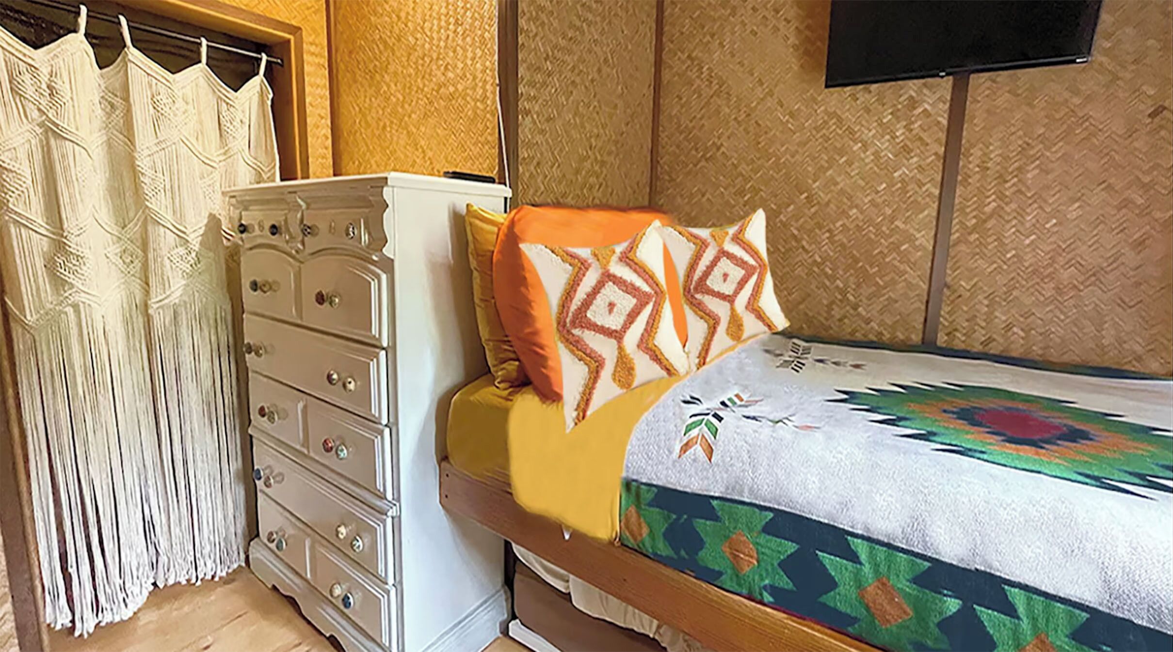 Un dormitorio con una cama, un aparador y una televisión en la pared.