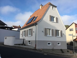 Ein zweistöckiges Haus mit einem geneigten Dach, Solaranlagen und Fensterläden.