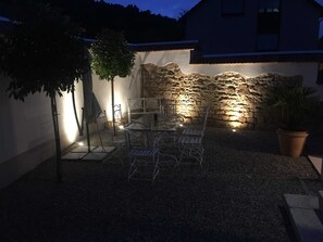 An outdoor patio with a stone wall, metal chairs, and a table.