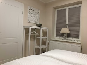 A bedroom with two beds, a radiator, a window with blinds, a white wardrobe, and a decorative wall piece.