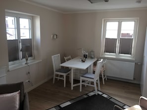A room with a white table, four chairs, a lamp, a radiator, and a window with blinds.