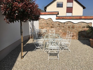 A patio with a metal table and chairs, a tree, and a stone wall.