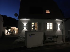 A house with a well-lit exterior, a satellite dish, and a small outdoor seating area.