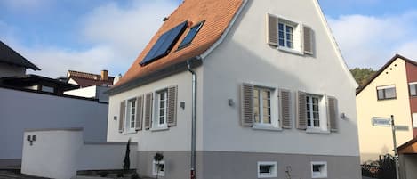 A two-story house with a sloped roof, solar panels, and shutters.