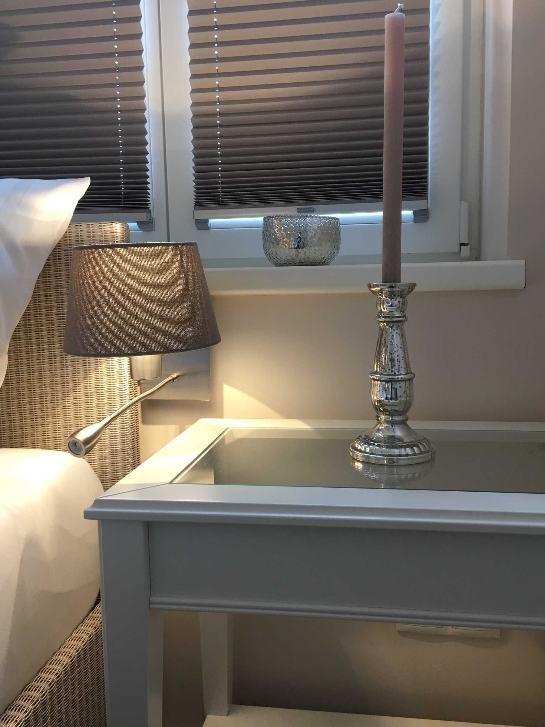 A bedside table with a glass top, a candle, and a lamp.