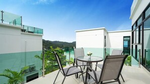 Un patio moderno al aire libre con una mesa redonda y sillas, rodeado de barandas de vidrio y follaje.