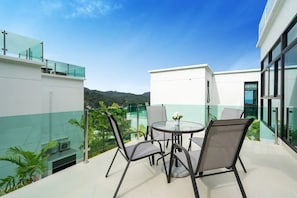 Une terrasse extérieure moderne, dotée d’une table ronde et de chaises, entourée de rampes en verre et de verdure.