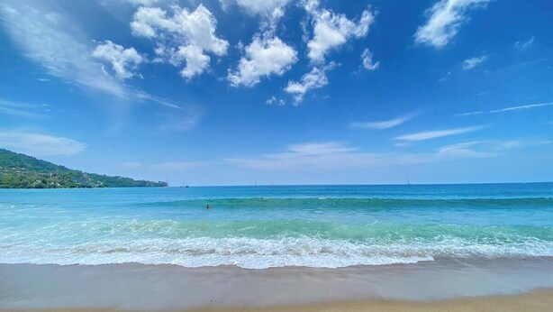 Una playa con agua azul cristalina, una orilla arenosa y una vista distante de un paisaje montañoso.