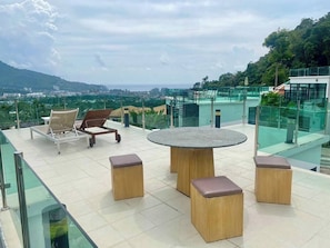 Enjoy panoramic views of the city and lush greenery from this rooftop terrace with a round table and comfortable seating.