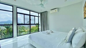 Un hotel moderno con una cama grande, un ventilador de techo y vistas de la ciudad a través de amplias ventanas.