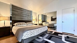 Un dormitorio moderno con una cama grande, mesitas de noche, un espejo y una puerta.