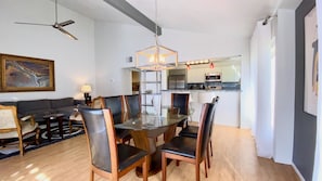 Una sala de estar moderna con una mesa de comedor, sillas, un sofá, un ventilador de techo y una zona de cocina con microondas y estufa.