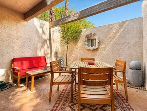 An outdoor patio with a wooden table and chairs, a red sofa, and a decorative mirror on the wall.