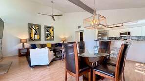 A modern living room with a dining area, a ceiling fan, and a kitchen with stainless steel appliances.