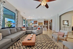 A modern living room with a sectional sofa, a coffee table, and a dining area with a kitchen in the background.